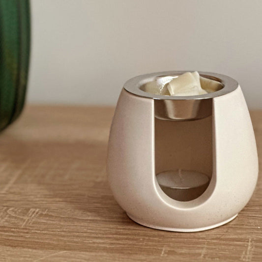 Brûleur à fondants Aura en matière minérale, posé sur une table en bois, ambiance cocooning et décoration intérieure chaleureuse