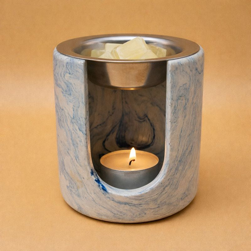 Brûleur à fondants parfumés en composite minéral marbré bleu et blanc, forme cylindrique, avec coupelle en inox et bougie chauffe-plat allumée