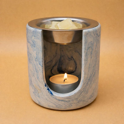 Brûleur à fondants parfumés en composite minéral marbré bleu et blanc, forme cylindrique, avec coupelle en inox et bougie chauffe-plat allumée
